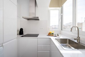 A modern kitchen with white cabinetry, a stainless steel sink, a black coffee maker, and a window providing a view of buildings outside.