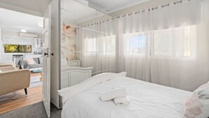 Une chambre moderne avec un grand lit, une table de chevet et une vue sur la cuisine par une porte ouverte.