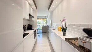 A narrow, modern kitchen with white cabinetry, a central island, and a view into a living area.