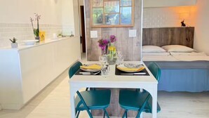 A modern kitchen with a dining area, a bed, and a bedside table with a lamp.