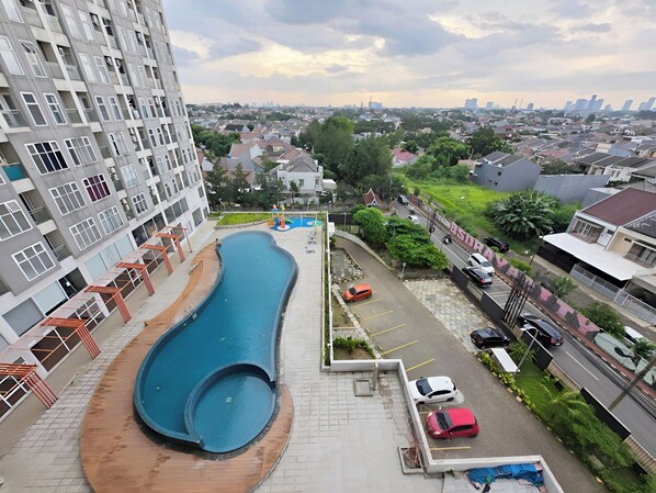 Un barrio residencial con piscina, coches aparcados y un edificio alto al fondo.