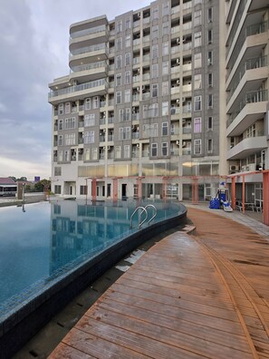 A modern apartment building with a rooftop swimming pool and wooden deck.