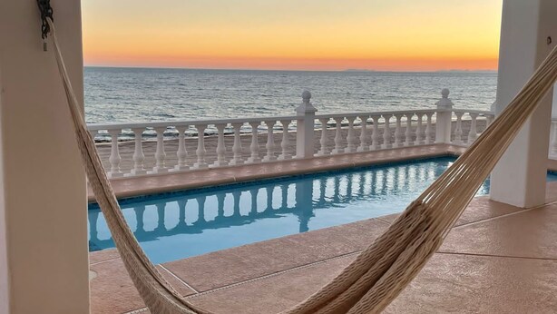 Un'amaca sopra una piscina con vista sull'oceano al tramonto.