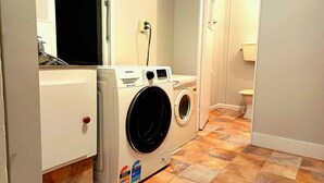 Un lavadero con lavadora y secadora de carga frontal, piso de baldosas y puerta que da a un baño.