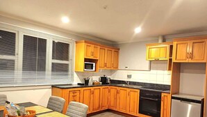 Una cocina moderna con armarios de madera, un microondas integrado, un lavavajillas de acero inoxidable y un comedor con mesa y sillas.