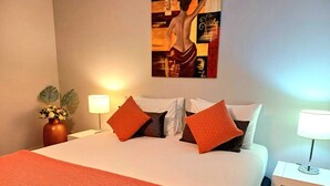 Habitación de hotel con una cama grande, dos mesitas de noche, una lámpara de noche, un jarrón con flores y un cuadro en la pared.