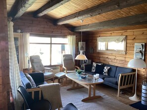 A cozy cabin interior with a wooden ceiling, a sofa, chairs, a table, and a window with curtains. - 6 Person Holiday Home in Henne (Henne)