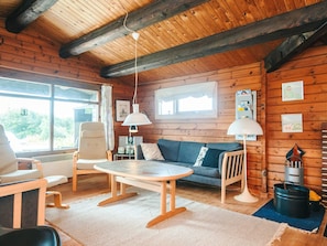 Interior acogedor de una cabaña con techo de madera, una mesa redonda, un sofá y una silla.