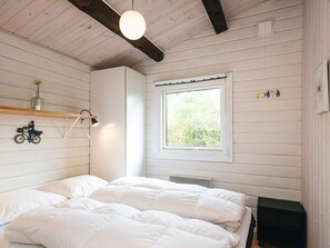 A bedroom with a bed, a window with a view of greenery, a shelf with decorative items, and a wall-mounted lamp.