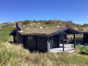 A small, rustic cabin with a thatched roof, a brick chimney, and a wooden deck. - 6 Person Holiday Home in Henne (Henne)