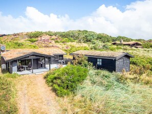 A modern house with a large deck and a covered outdoor area, surrounded by natural vegetation and hills. - 6 Person Holiday Home in Henne (Henne)