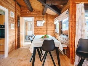 Interior de una cabaña de madera con una mesa de comedor, sillas y una ventana con cortinas.