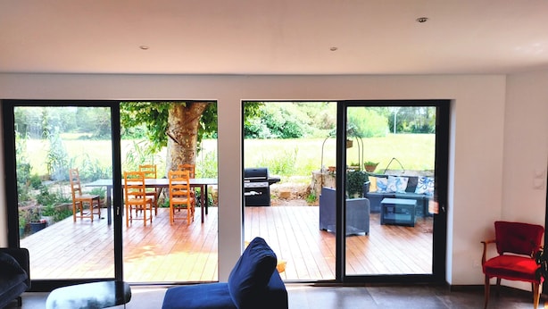 A modern living room with a large sliding glass door leading to an outdoor patio. - Country house in Provence (Istres)