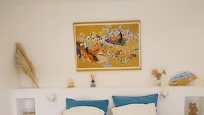 A bedroom with a bed, two pillows, a wall-mounted painting, and a small shelf with decorative items. - Country house in Provence (Istres)