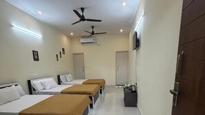 Une chambre d’hôtel avec trois lits, un ventilateur de plafond, un climatiseur et un téléviseur fixé au mur.