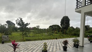 Un espace extérieur aménagé avec une surface pavée, des plantes en pot et une vue sur un champ verdoyant et des arbres en arrière-plan.