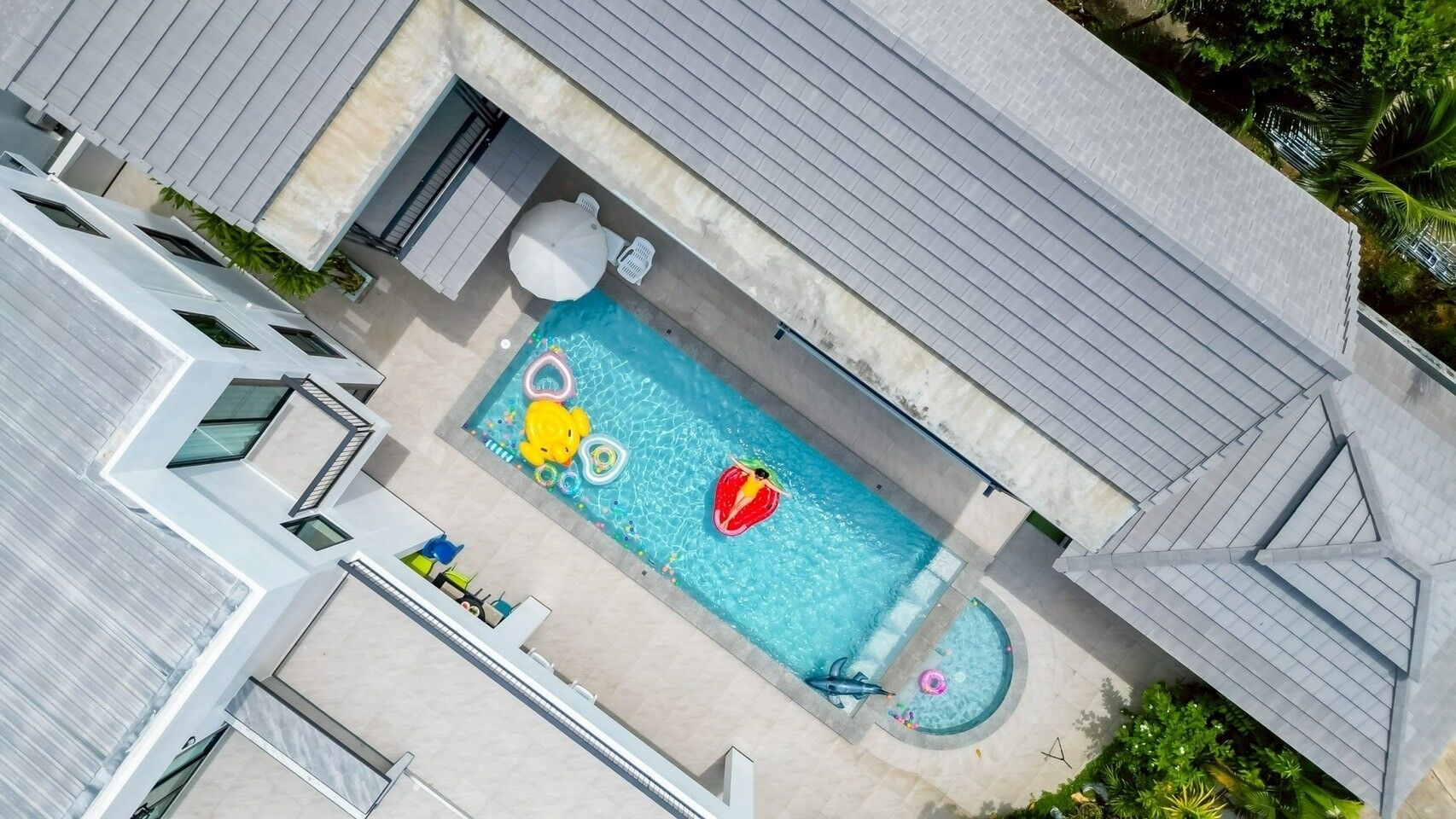 Vista aérea de una casa moderna con piscina rectangular, un porche cubierto y una pequeña terraza con asientos.