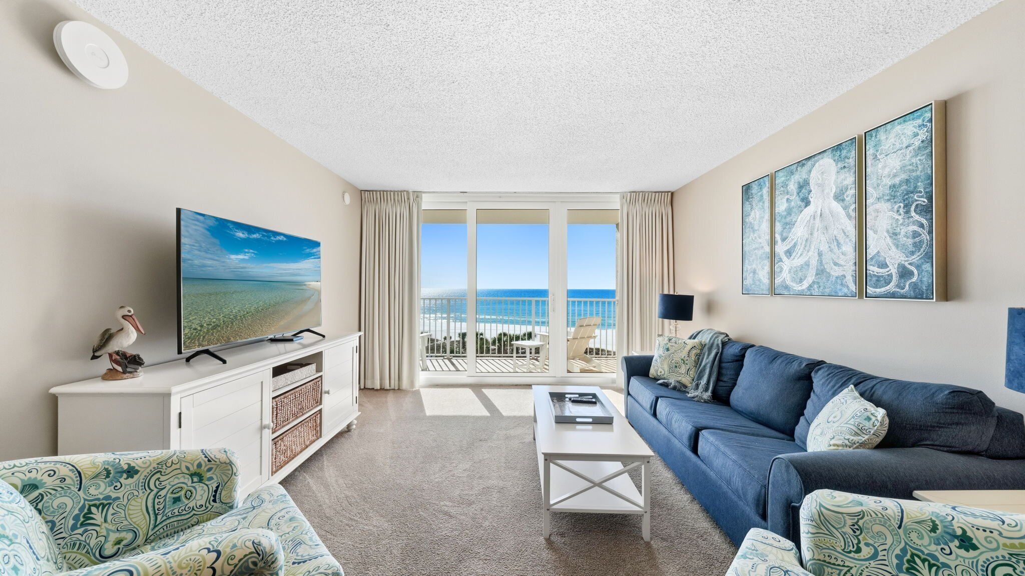 Ein großzügiges Wohnzimmer mit großem Fernseher, bequemen Sitzgelegenheiten und einem Balkon mit Meerblick.