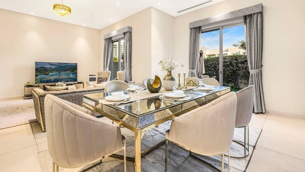 A modern dining room with a glass-top table, beige upholstered chairs, and a chandelier. - Stylish 4BR Family Villa – Easy Access to Dubai Marina & Expo City (Dubai)
