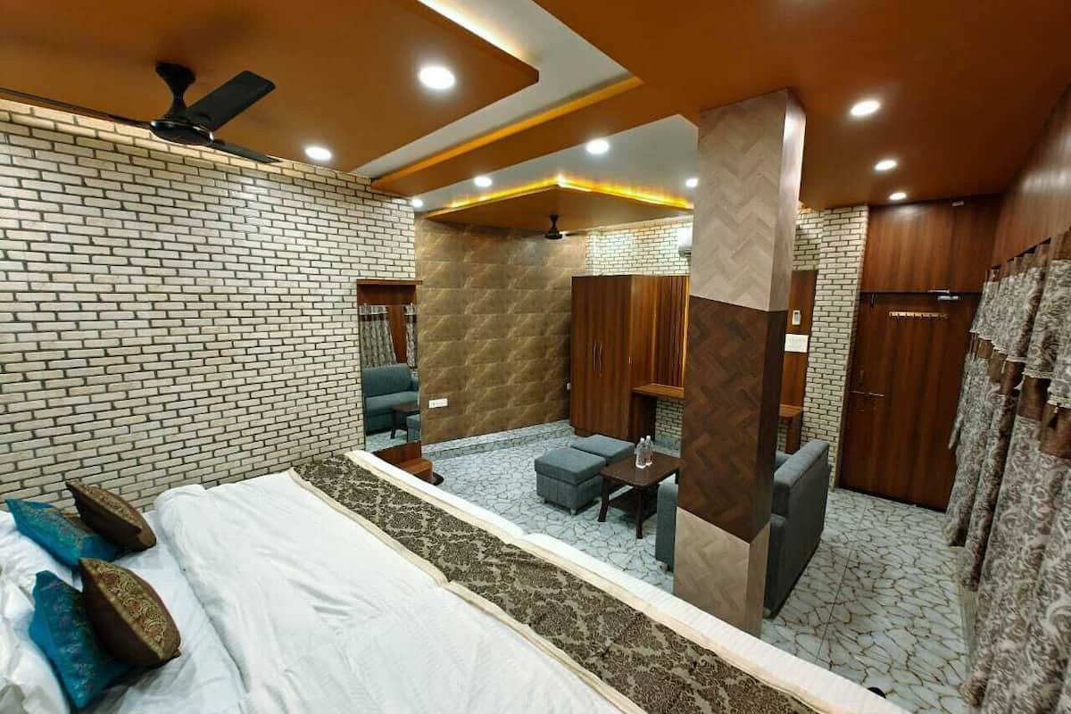 Una camera d'hotel con parete a mattoni, un letto con cuscini, un angolo relax con un tavolo e mobili contenitori in legno.
