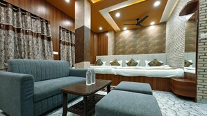 A modern hotel room with a sofa, a bed with decorative pillows, a small table with water bottles, and a ceiling fan. - kailash pati guest house (Varanasi)