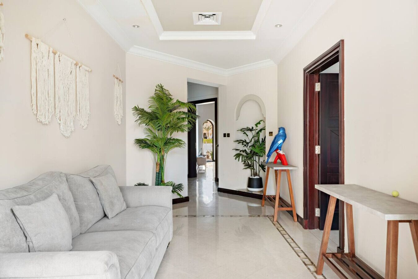 Un salon moderne avec un canapé gris, une décoration murale en macramé et une plante en pot.