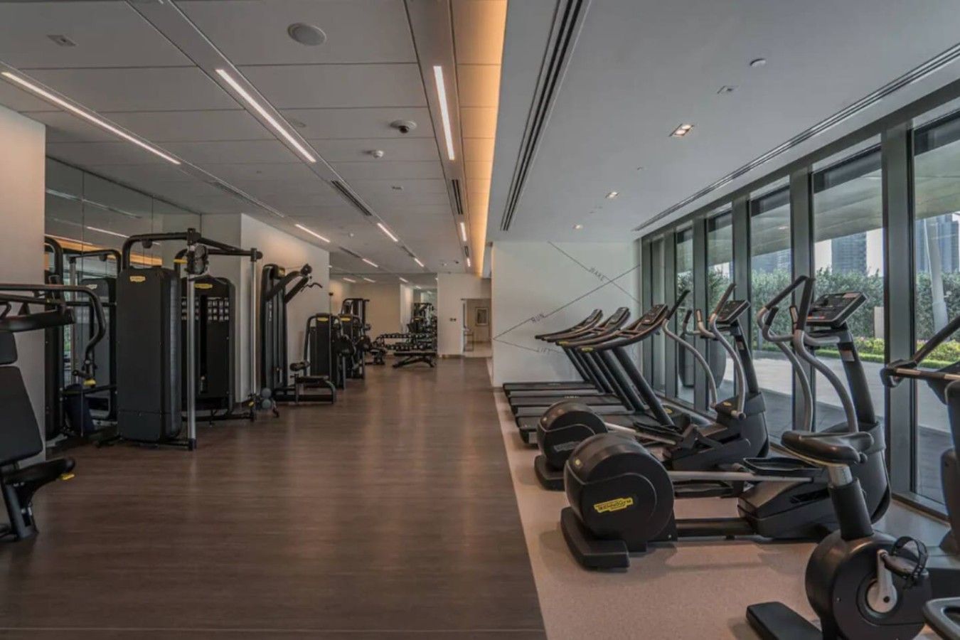 Een sportschool met cardioapparatuur, krachttoestellen en een spiegelwand.