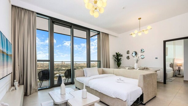 A modern living room with a sofa, coffee table, and dining area. Large windows offer a city view.
