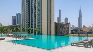 A rooftop swimming pool with lounge chairs and a view of high-rise buildings.