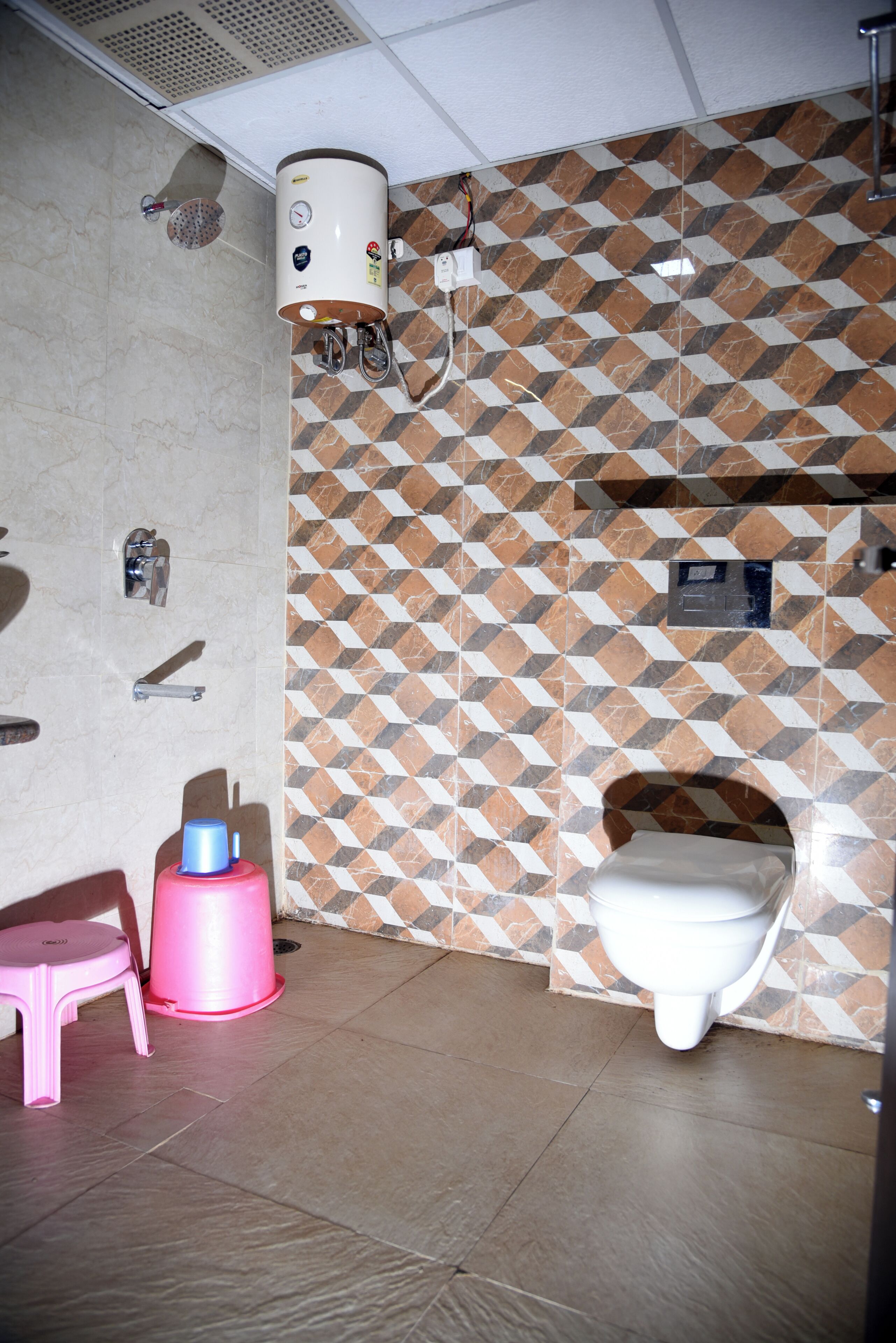 A bathroom with a patterned tile wall, a toilet, a pink trash bin, and a water heater.