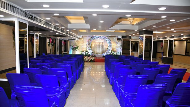 A conference room with rows of blue chairs, a floral backdrop, and a chandelier. - SVR HOTEL & BANQUET PATNA (Patna)