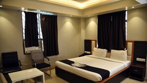 Habitación de hotel con una cama grande, un escritorio, dos sillas, una mesita de noche y una ventana con cortinas.