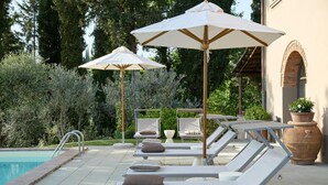 A poolside area with lounge chairs and umbrellas, a pool, and a building with an arched window. - Lovely home in Terranuova Bracciolini (Terranuova Bracciolini)