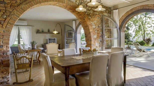 A dining area with a stone archway, wooden table, and chairs. There is a view of the outdoors through large windows. - Lovely home in Terranuova Bracciolini (Terranuova Bracciolini)