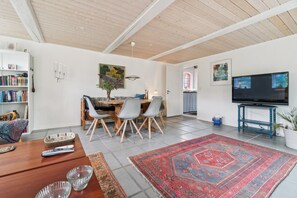 A modern living room with a dining area, a flat-screen TV, and a bookshelf.