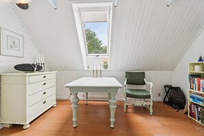 A room with a white table, a chair, a dresser, a bookshelf, and a window.