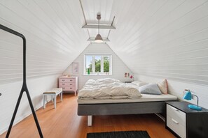A bedroom with a sloped ceiling, a bed, a dresser, a nightstand, a window, and a black floor lamp.