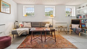 A living room with a sofa, coffee table, and a bookshelf. - Scenic area close to forest, golf, and beach (Rønne)