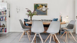 A dining area with a wooden table, grey chairs, a white pendant light, and a painting on the wall. - Scenic area close to forest, golf, and beach (Rønne)