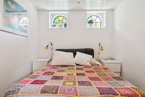A bedroom with a large bed, two bedside tables, a headboard, and two windows with plants. - Scenic area close to forest golf and beach (Rønne)