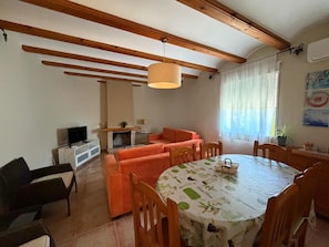 A room with a fireplace, orange sofa, dining table with chairs, and a television on a stand.