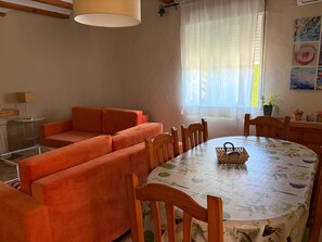 Une pièce comprenant un canapé, une table à manger, des chaises, une lampe et une fenêtre avec des rideaux.