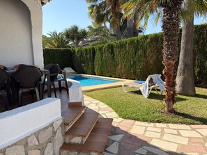 A poolside area with a stone staircase, lounge chairs, and a dining setup.