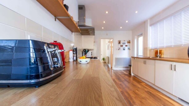 Une cuisine moderne avec un plancher en bois, des armoires intégrées, un appareil électroménager noir et rouge, et un comptoir blanc.