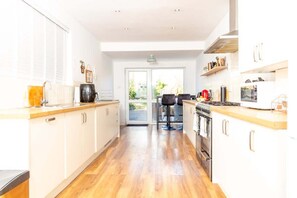 A modern kitchen with white cabinets, a wooden countertop, a stove, and a dining area with two chairs. - Charming Getaway: 3BR Home in the Heart of Chester (Chester)