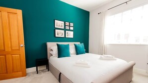 Une chambre à coucher avec un lit, une table de chevet, une fenêtre avec des rideaux et un mur de couleur turquoise.