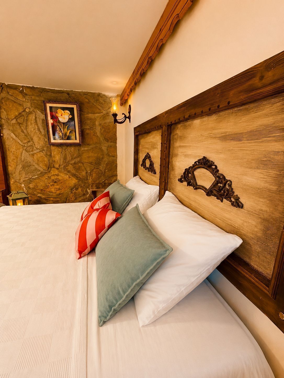 A neatly made bed with pillows, a framed picture on the wall, and a stone wall.