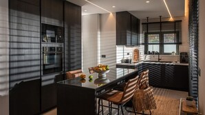 A modern kitchen with a central island, dark cabinetry, and a dining area with chairs and a table.