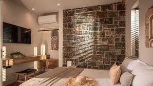 A bedroom with a stone wall, a bed with pillows, a bedside table, and a TV mounted on the wall.
