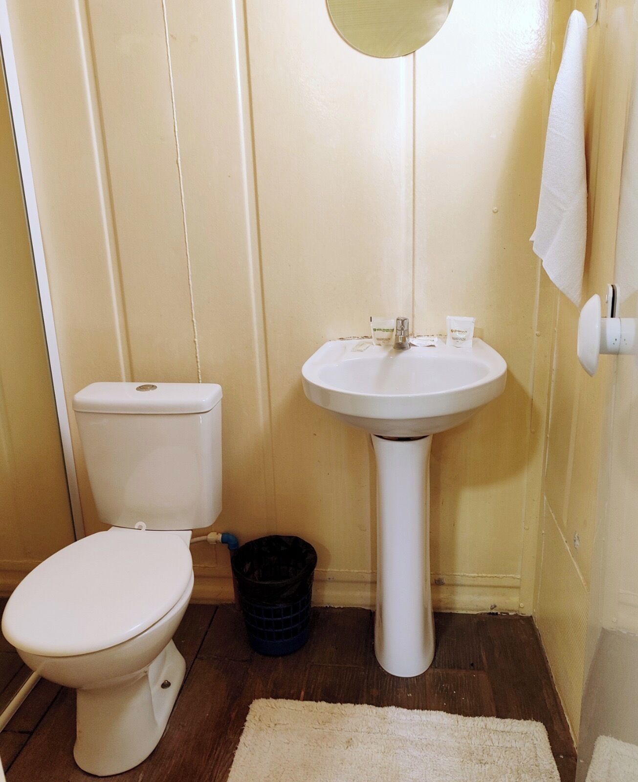 Un baño pequeño con inodoro, lavamanos y un cubo de basura negro.